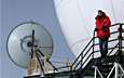 USAP participant Nick Powell stands next to a communications satellite dish at South Pole Station.