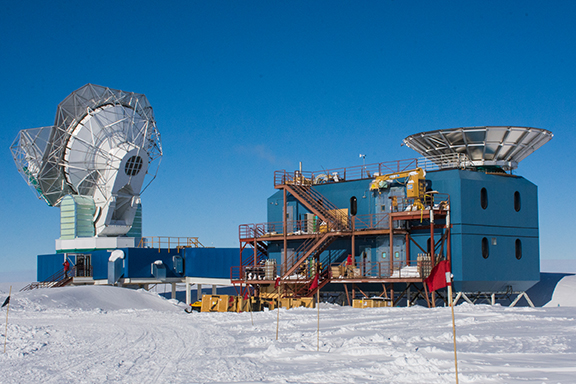 A large telescope sits at the end of a building with a large dish at the opposite end.