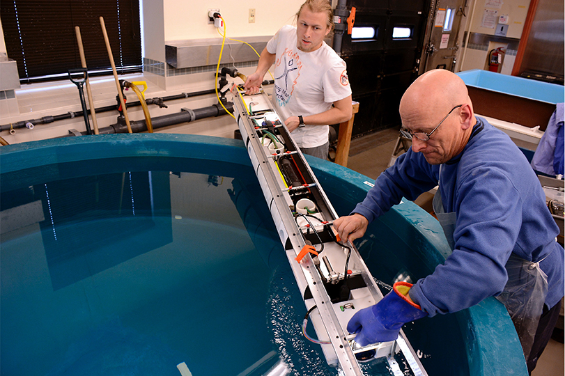 Two people place scientific instrument in a pool of water.