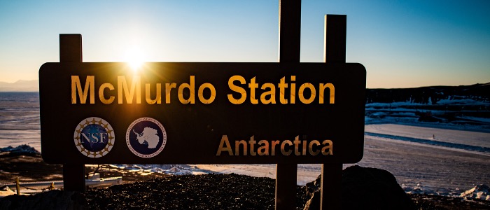 A late day sun backlights a large sign for McMurdo Station.
