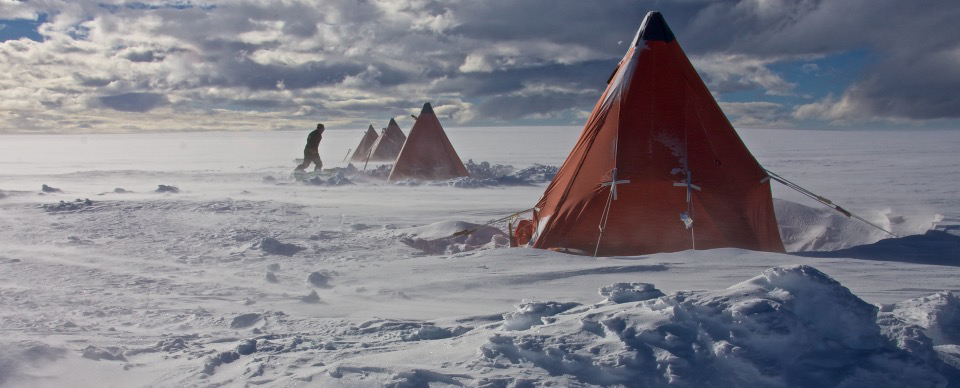 Red tents sit in a row on snow with a person walking