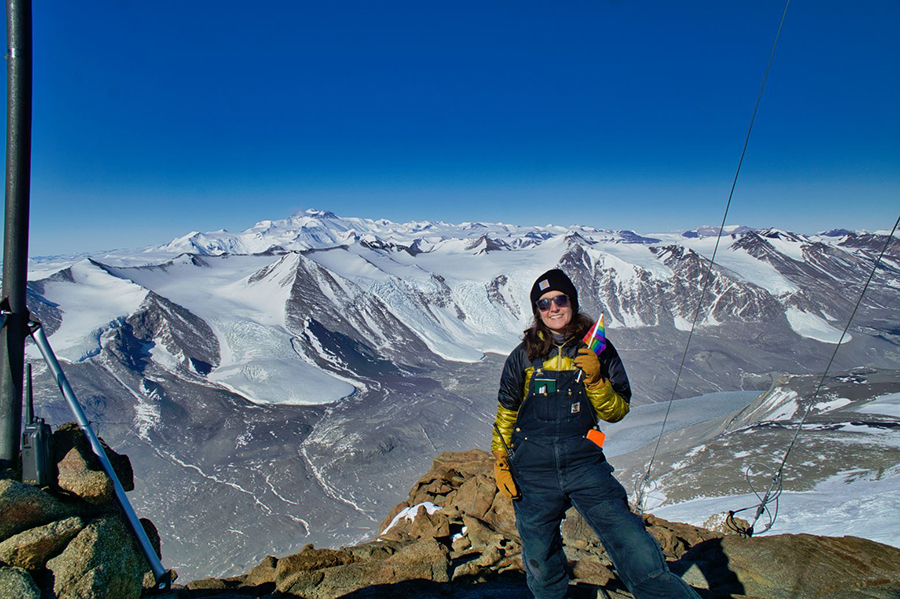 Becky Carson, part of the USAP radio communications team, holds a pride flag on a mountaintop near Taylor Valley as her team works to provide internet data connectivity to science groups and support staff working in the McMurdo Dry Valleys.